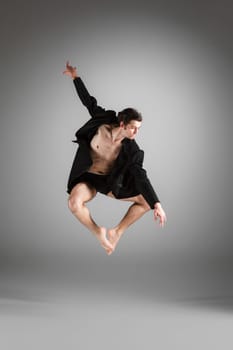 The young attractive modern ballet dancer in black jacket  jumping over gray background