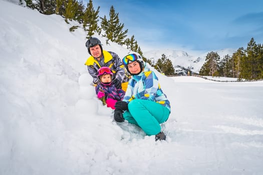 Family, mother, father and daughter, build a small snowman next to ski slope. Ski winter holidays in Andorra, El Tarter, Pyrenees Mountains