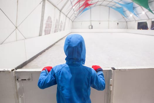 Child boy observes a temporary skating rink installed for Christmas holidays