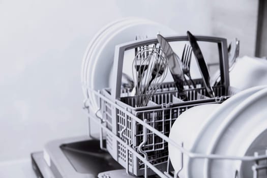 Front view of open automatic stainless steel built-in fully integrated top control dishwasher range machine with clean utensils, cutlery, glasses, dishes, plates inside in modern home kitchen