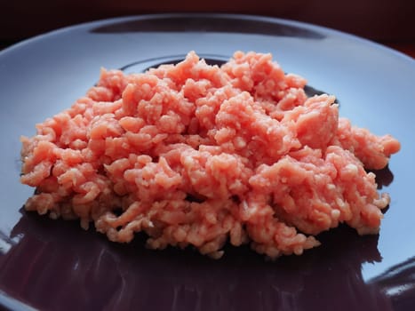 Minced meat on a purple ceramic large plate. Delicious fresh ground meat for making cutlets, steaks, hamburgers, meatballs. Pork semi-finished products.