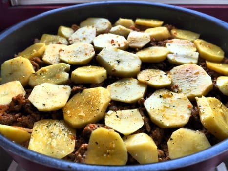 Raw potatoes, cut into circles and stacked on top of minced meat and onions. Moussaka making process. Spices on potatoes. Balkan cuisine - traditional Greek, Serbian and Turkish food.