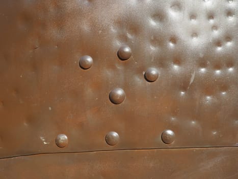 Metal surface with rivets and bolts. Abstract background of a military or industrial nature. Sheathing with dents, seams and nuts. Fasteners on metal. Steel or bronze panel.