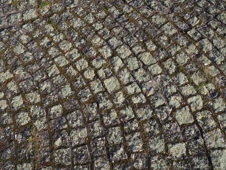 Neatly laid out old paving stones. Pavement on the square of the old town. Square and rectangular stones on the ground, covered with moss and lichens.