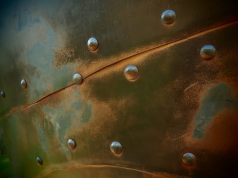 Metal surface with rivets and bolts. Abstract background of a military or industrial nature. Sheathing with dents, seams and nuts. Fasteners on metal. Steel or bronze panel.