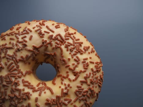 A doughnut or donut. A type of leavened fried dough. Sweet snack that can be homemade or purchased in bakeries, supermarkets, food stalls. Delicious pie with light icing on a dark gray background.