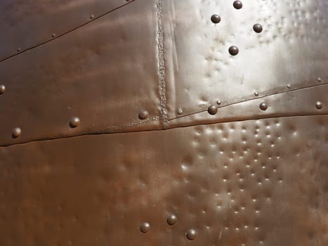 Metal surface with rivets and bolts. Abstract background of a military or industrial nature. Sheathing with dents, seams and nuts. Fasteners on metal. Steel or bronze panel.