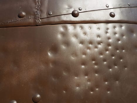 Metal surface with rivets and bolts. Abstract background of a military or industrial nature. Sheathing with dents, seams and nuts. Fasteners on metal. Steel or bronze panel.
