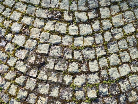 Neatly laid out old paving stones. Pavement on the square of the old town. Square and rectangular stones on the ground, covered with moss and lichens.