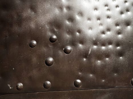 Metal surface with rivets and bolts. Abstract background of a military or industrial nature. Sheathing with dents, seams and nuts. Fasteners on metal. Steel or bronze panel.