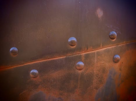 Metal surface with rivets and bolts. Abstract background of a military or industrial nature. Sheathing with dents, seams and nuts. Fasteners on metal. Steel or bronze panel.