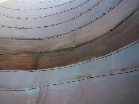 Metal surface with rivets and bolts. Abstract background of a military or industrial nature. Sheathing with dents, seams and nuts. Fasteners on metal. Steel or bronze panel.