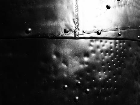 Metal surface with rivets and bolts. Abstract background of a military or industrial nature. Sheathing with dents, seams and nuts. Fasteners on metal. Steel or bronze panel.