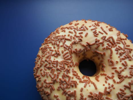 A doughnut or donut. A type of leavened fried dough. Sweet snack that can be homemade or purchased in bakeries, supermarkets, food stalls. Delicious pie with light icing on a blue background.