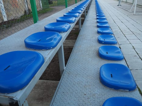 Seats and benches on the sports ground. Plastic blue seats for spectators and fans, empty, no people.