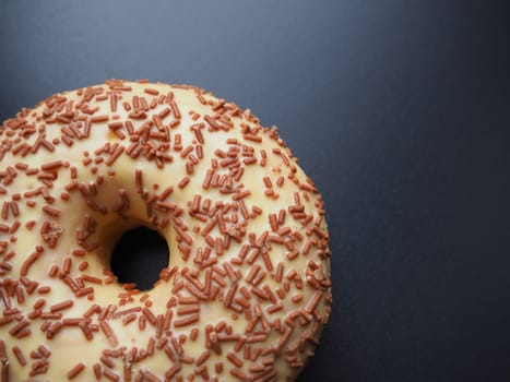 A doughnut or donut. A type of leavened fried dough. Sweet snack that can be homemade or purchased in bakeries, supermarkets, food stalls. Delicious pie with light icing on black or gray background.