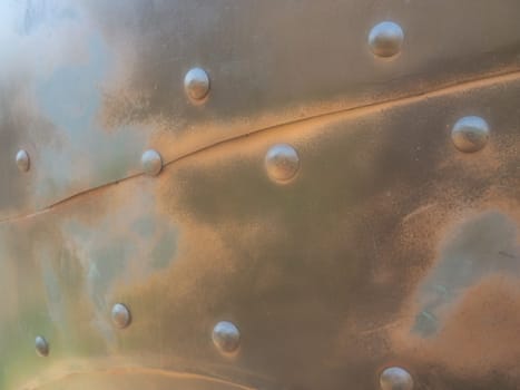 Metal surface with rivets and bolts. Abstract background of a military or industrial nature. Sheathing with dents, seams and nuts. Fasteners on metal. Steel or bronze panel.