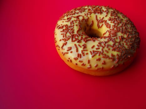 A doughnut or donut. A type of leavened fried dough. Sweet snack that can be homemade or purchased in bakeries, supermarkets, food stalls. Delicious pie with light icing on a red background.