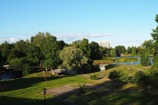 Mouth, floodplain and terraces of the Lososinka River, Petrozavodsk, Republic of Karelia August 3, 2022. Sunny windless evening. Bushes and trees. Passers-by people cross the river through the bridge