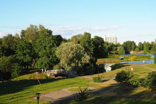 Mouth, floodplain and terraces of the Lososinka River, Petrozavodsk, Republic of Karelia August 3, 2022. Sunny windless evening. Bushes and trees. Passers-by people cross the river through the bridge