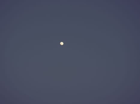 Moon in the night blue sky. White point in the sky. Dark vignetting around the edges of the image