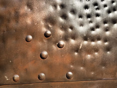 Metal surface with rivets and bolts. Abstract background of a military or industrial nature. Sheathing with dents, seams and nuts. Fasteners on metal. Steel or bronze panel.