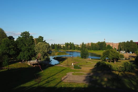 Mouth, floodplain and terraces of the Lososinka River, Petrozavodsk, Republic of Karelia August 3, 2022. Sunny windless evening. Bushes and trees. Passers-by people cross the river through the bridge