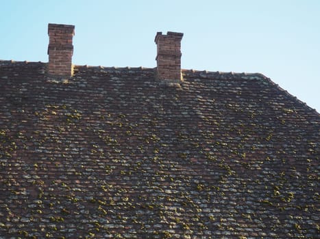 Tiled roof with twin tailpipes. Old tiles with moss and lichens on the roof of a residential building. Heating buildings with wood and coal.