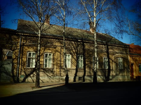 Sremska Mitrovica, Serbia, February 15, 2021. Facade of old houses of the 19-20 century. Historical architectural value. Ornate stucco houses in the streets of the city. Birch trees on the lawn