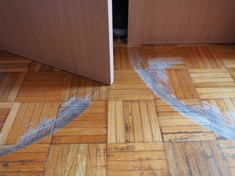 Scratched parquet flooring in the room. Scratches, chips and dents on the floor. Parquet in need of repair. Cabinet doors are scratching the floor. Unadjusted height of furniture doors.