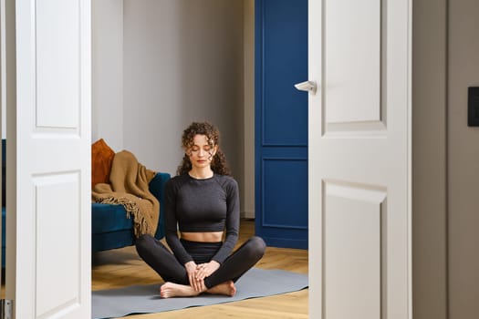 Beautiful happy girl with closed eyes practicing yoga in lotus position at home