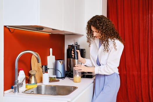 Woman using electric blender to make hummus at home