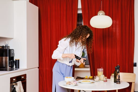 Woman with curly hair sprinkles ground pepper on plate with hummus