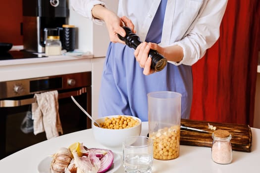 Closeup view of adding pepper into blender with chickpeas while making hummus