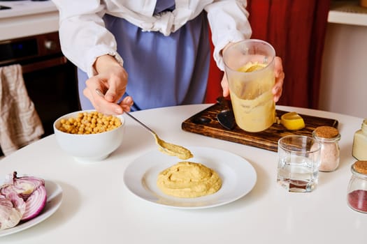 Unrecognizable woman puts hummus on a plate. Handmade fresh food.