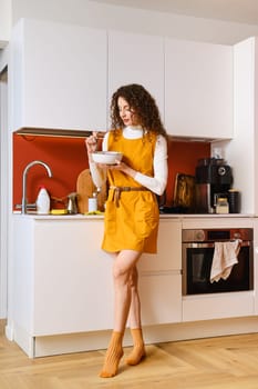 Slim woman eating salad in a hurry standing in the kitchen