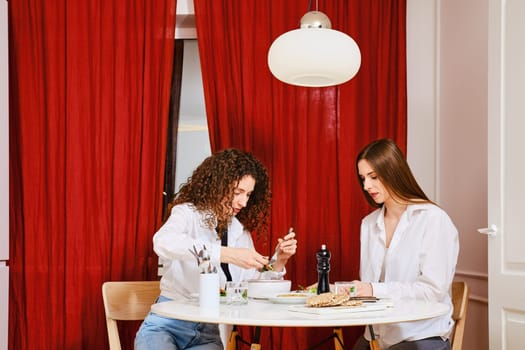 Young woman dining with her friend puts probiotic salad in her plate