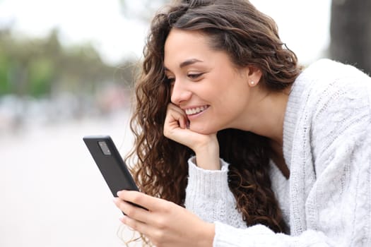 Happy woman using cell phone outdoors in the street