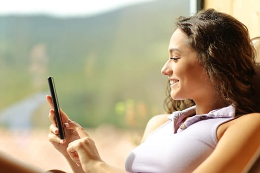 Happy woman using cell phone on a chair at home