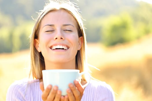 Front view portrait of a happy teen breathing fresh air holding coffee cup in the mountain