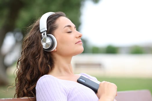 Relaxed woman resting in a bench listening music