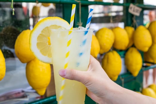 Caucasian hand with healthy fresh lemonade during summer with lemons background