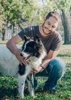 Man with his dog playing outdoor in the park. Young owner hugs his pet in nature.