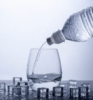 Pouring fresh drinking mineral water from plastic bottle. Glass filled with water over white background.