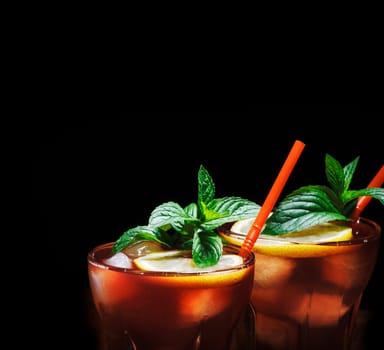 Cuba libre cocktail with ice, mint and lemon over black background. Alcohol beverage with rum and cola drink. Cocktail design menu background.