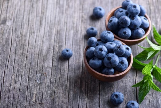 Bowl of fresh blueberries on rustic wooden table. Healthy organic seasonal fruit background. Organic food blueberries and mint leaf for healthy lifestyle.