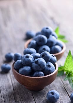 Bowl of fresh blueberries on rustic wooden table. Healthy organic seasonal fruit background. Organic food blueberries and mint leaf for healthy lifestyle.
