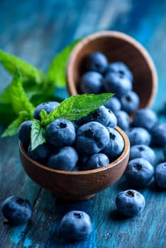 Bowl of fresh blueberries on rustic wooden table. Healthy organic seasonal fruit background. Organic food blueberries and mint leaf for healthy lifestyle.