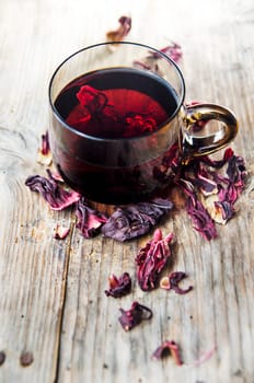 Hibiscus tea in teacup with dry hibiscus flower leaves. Organic herbal cup of tea on vintage wooden table background.