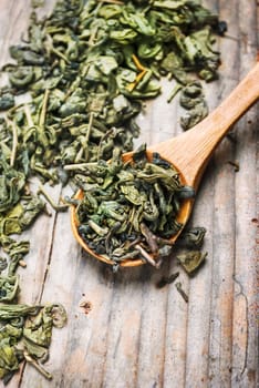 Dry green tea leaves in wooden spoon from above. Organic asian green herbal tea on vintage wooden table background.